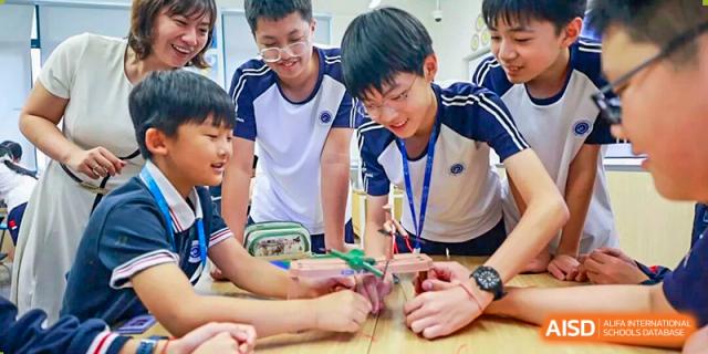 A male student and his classmates happily work on a small engineering project with balsa wood and tools in a classroom at BASIS International School Park Lane Harbour.