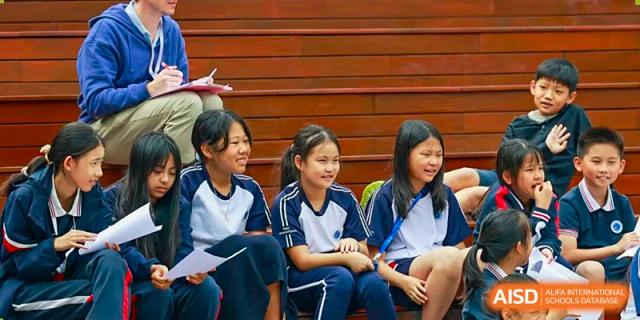 Three high school girls in navy and white uniforms smiling while sitting and holding papers during an indoor event at BASIS International School Park Lane Harbour.