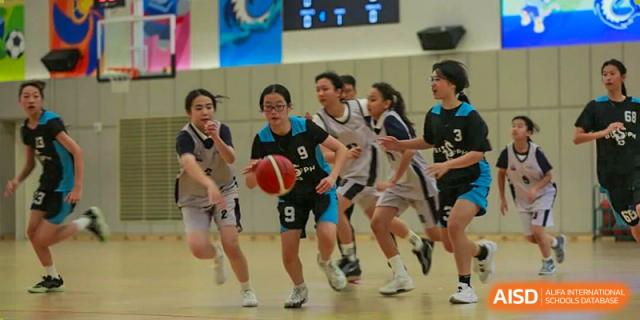 A group of students playing a competitive basketball game indoors, with one student dribbling the ball at BASIS International School Park Lane Harbour.