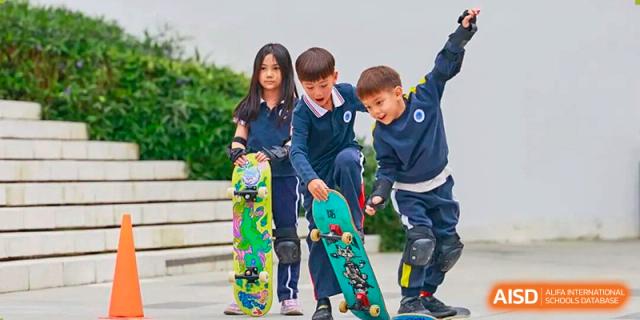 Three children in school uniforms are standing outdoors with skateboards and protective gear at BASIS International School Park Lane Harbour.