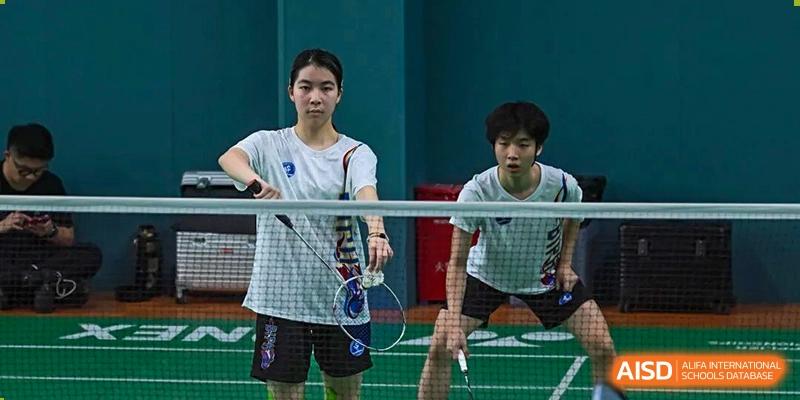 Two students are playing badminton indoors, standing ready on the court with rackets in hand at BASIS International School Park Lane Harbour.