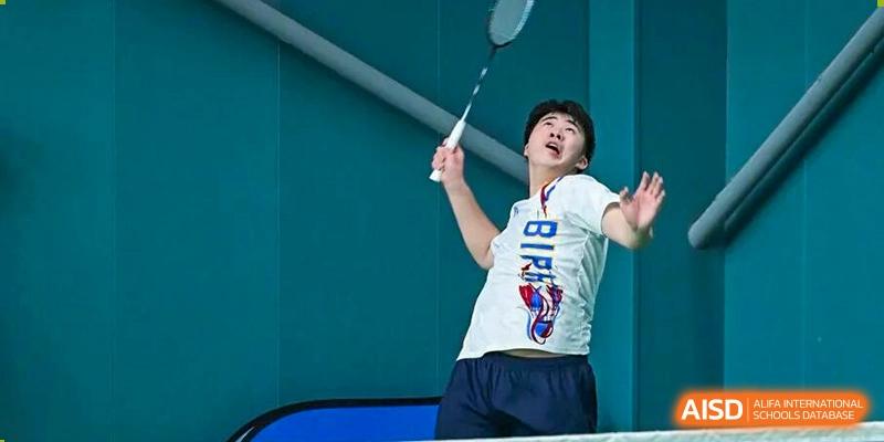 A student in a white shirt is hitting a shuttlecock during an energetic badminton match indoors at BASIS International School Park Lane Harbour.
