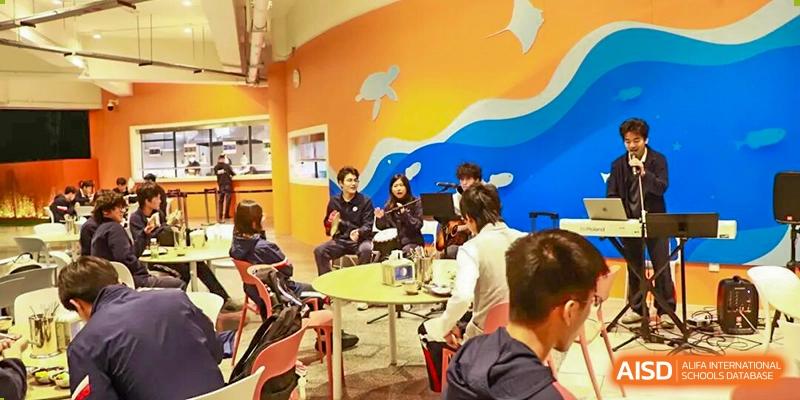 Students are gathered in a colorful common room, sitting and talking at small tables at BASIS International School Park Lane Harbour.