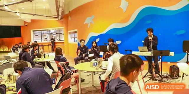 Students are gathered in a colorful common room, sitting and talking at small tables at BASIS International School Park Lane Harbour.