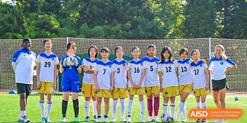 A girls' soccer team is lined up and posing for a team photo on the green field outdoors at BASIS International School Park Lane Harbour.