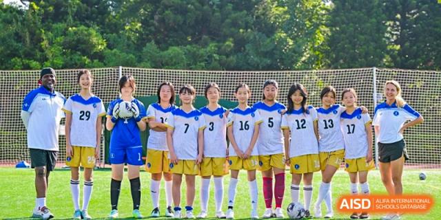 A girls' soccer team is lined up and posing for a team photo on the green field outdoors at BASIS International School Park Lane Harbour.