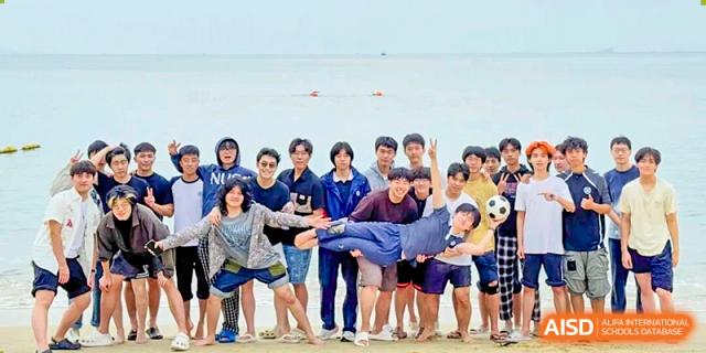 A group of students and a teacher are on a beach, collectively lifting one of the adults in the air, representing a team activity at BASIS International School Park Lane Harbour.