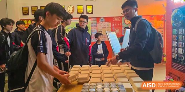 Students in a classroom setting working together to organize and package boxed meals and canned goods for a service project at BASIS International School Park Lane Harbour.