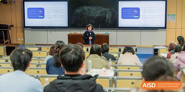 A teacher standing near a large screen in a lecture hall addressing a classroom full of students seated in rows at Nanjing Foreign Language School.