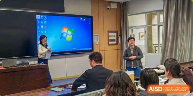 A small group of teachers or staff is gathered in a room, watching a presentation on a large wall-mounted screen displaying a Windows logo, a setup used at Nanjing Foreign Language School.