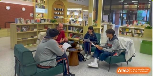 A teacher or mentor is sitting on the floor with several students in a library or reading corner for a small-group, informal study session at the Nanjing Foreign Language School.