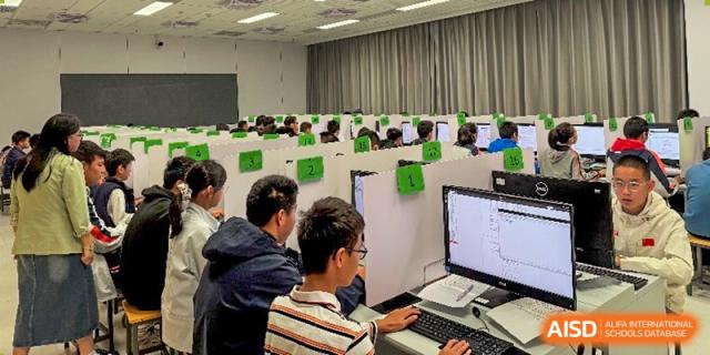 Students are seated at individual computer stations in a lab, working on desktop computers, likely for research or coding practice sessions at Nanjing Foreign Language School.