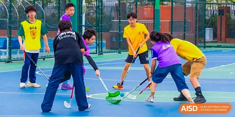 Students are engaged in a game of floor hockey, with several players chasing the ball and others watching, highlighting energetic sporting activities within Nanjing Foreign Language School.
