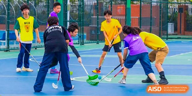 Students are engaged in a game of floor hockey, with several players chasing the ball and others watching, highlighting energetic sporting activities within Nanjing Foreign Language School.