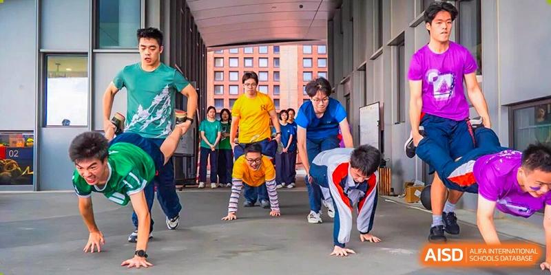 Male students are competing in a push-up or crawling race drill on a paved court during an indoor/outdoor activity, demonstrating physical education and teamwork at Nanjing Foreign Language School.