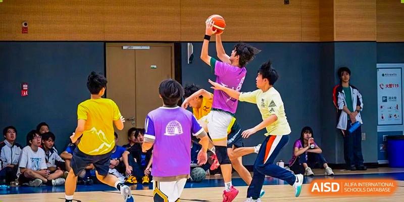 Students are actively playing a basketball-like game on an indoor court, with one student jumping to shoot or block the ball, showcasing dynamic school athletics at Nanjing Foreign Language School.