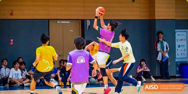 Students are actively playing a basketball-like game on an indoor court, with one student jumping to shoot or block the ball, showcasing dynamic school athletics at Nanjing Foreign Language School.