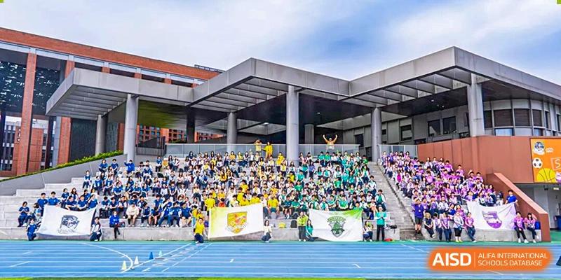 A large group of spectators in yellow and green shirts is filling the stadium bleachers next to a blue track during a sporting event or rally under an overcast sky at Nanjing Foreign Language School.