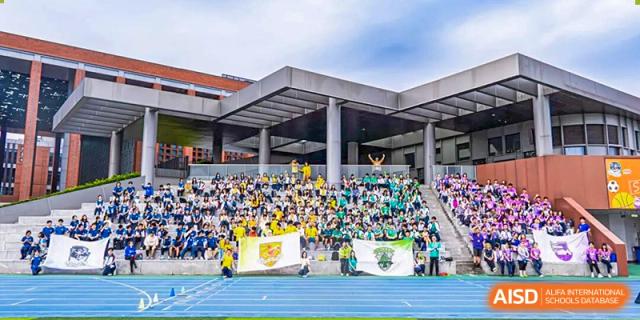 A large group of spectators in yellow and green shirts is filling the stadium bleachers next to a blue track during a sporting event or rally under an overcast sky at Nanjing Foreign Language School.