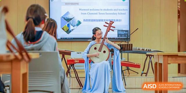 A female student in a traditional light blue dress playing a pipa (Chinese lute) on a stage during a performance at Nanjing Foreign Language School.