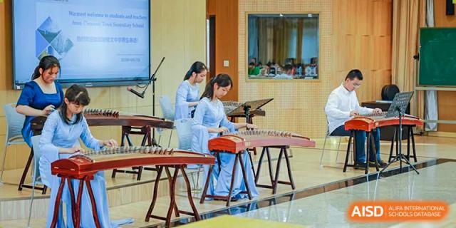 Two female students in matching light blue traditional attire playing Chinese zithers (guzheng) together indoors at Nanjing Foreign Language School.
