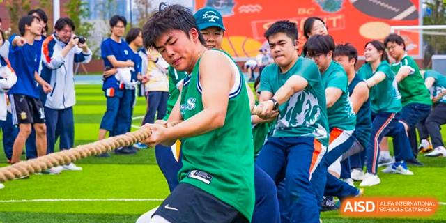 A group of students in green and white shirts intensely participating in a tug-of-war game, pulling the rope with effort at Nanjing Foreign Language School.