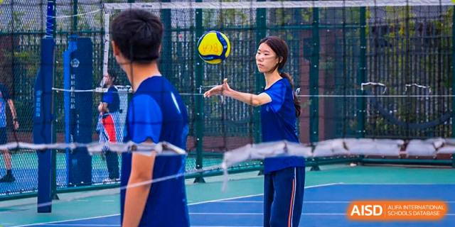 Two students in blue athletic wear interacting on an outdoor sports court or track, with nets visible in the background at Nanjing Foreign Language School.