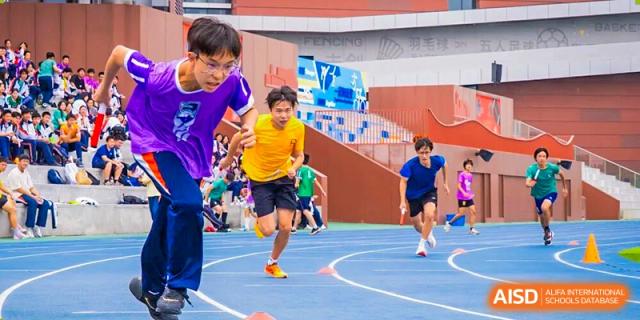 A young male student in a bright yellow shirt running fast on a blue track during a race or sports day event at Nanjing Foreign Language School.