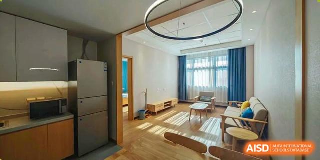 A bright, modern apartment's open living area with wooden floors, a small kitchen area, and natural light, potentially a staff residence provided by Nanjing Foreign Language School.
