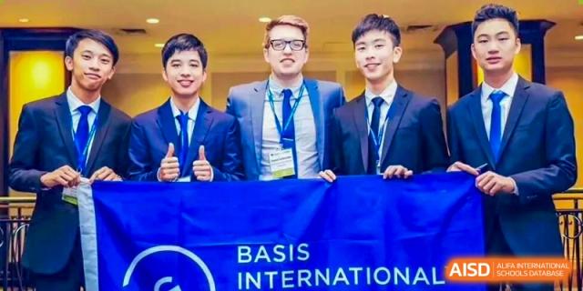 Three male students in formal suits stand proudly behind a blue "BASIS" banner at an academic event held at BASIS International School Shenzhen.