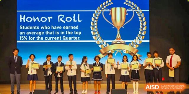 A group of elementary students stand on stage holding award certificates in front of an Honor Roll backdrop at BASIS International School Shenzhen.