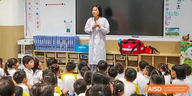 A teacher in a white lab coat presents a lesson to a classroom of seated young students during a science unit at BASIS International School Shenzhen.