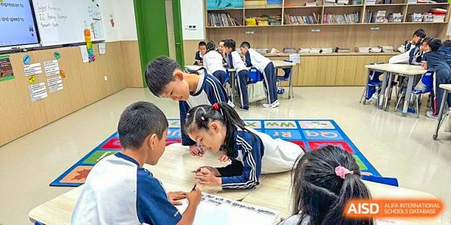 Two students collaborate on a writing assignment while kneeling on a colorful alphabet rug in a classroom at BASIS International School Shenzhen.