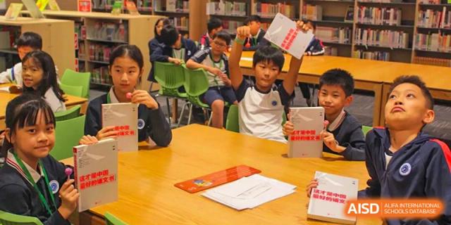 Students raise their hands and hold up books during an engaging classroom lesson in the library at BASIS International School Shenzhen.