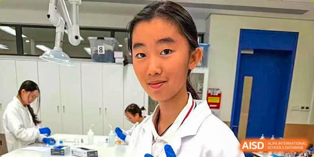 A female student wearing a white lab coat and blue gloves smiles during a science experiment at BASIS International School Shenzhen.