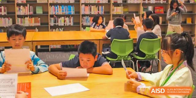 A young student focuses intently on reading a document while sitting at a wooden table in the library at BASIS International School Shenzhen.