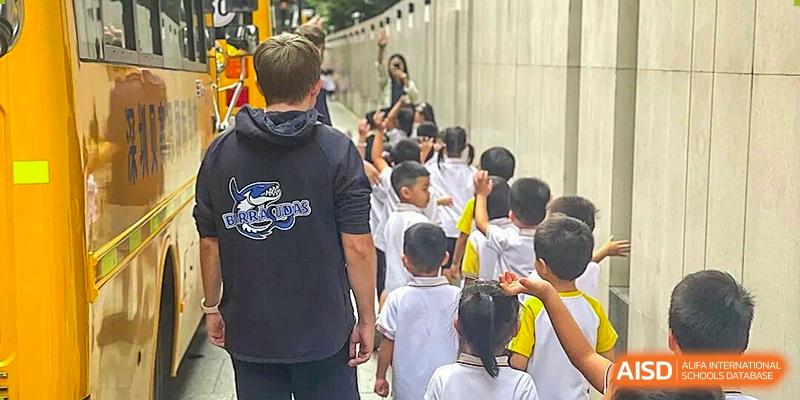 A teacher guides a line of students in white uniforms as they walk outdoors along a campus walkway at BASIS International School Shenzhen.