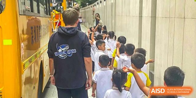 A teacher guides a line of students in white uniforms as they walk outdoors along a campus walkway at BASIS International School Shenzhen.