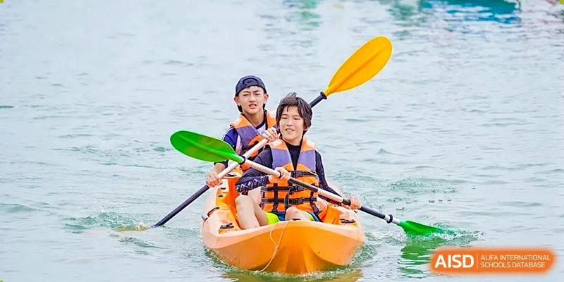 Two students in life jackets and helmets paddle an orange tandem kayak on the water during an outdoor activity at BASIS International School Shenzhen.