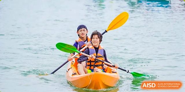 Two students in life jackets and helmets paddle an orange tandem kayak on the water during an outdoor activity at BASIS International School Shenzhen.