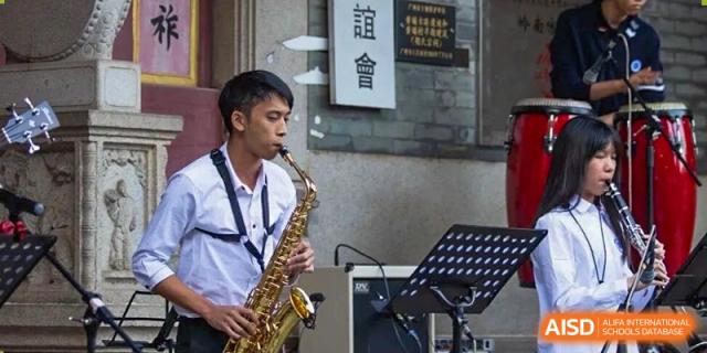 A student in a white shirt plays the saxophone outdoors during a performance at BASIS International School Shenzhen.