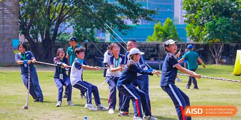 Students in school uniforms cheer and pull with effort during an outdoor tug-of-war match at BASIS International School Shenzhen.