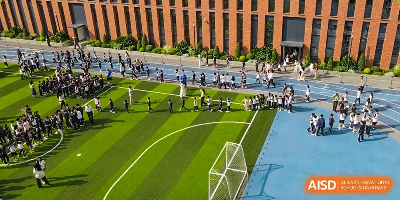 An aerial view of students lined up on a green turf sports field next to a brick building at BASIS International School Shenzhen.