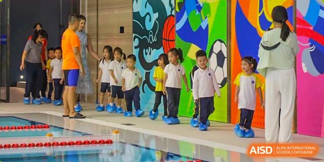 Young students wearing blue shoe covers walk in a line past a colorful mural near the pool at BASIS International School Shenzhen.
