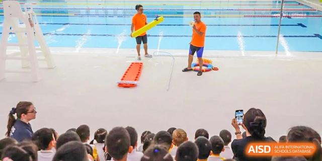 Instructors demonstrate water safety and rescue equipment to a group of seated students by the pool at BASIS International School Shenzhen.