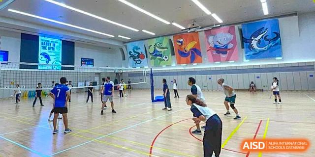 Students and staff engage in a competitive volleyball match inside a large, modern indoor court at BASIS International School Shenzhen.