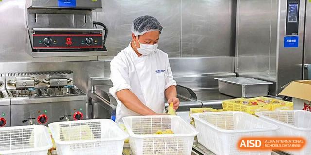 A cafeteria worker wearing a hairnet and mask prepares fresh food in a clean industrial kitchen at BASIS International School Shenzhen.