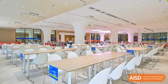 The modern, bright, and spacious school cafeteria features long wooden tables and white chairs at BASIS International School Shenzhen.