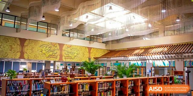 Rows of wooden bookshelves filled with various books are neatly organized inside a bright and spacious school library facility at Beijing City International School.