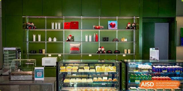 A variety of pastries and snacks are displayed behind a glass counter in a modern, green-walled school cafeteria or cafe area at Beijing City International School.